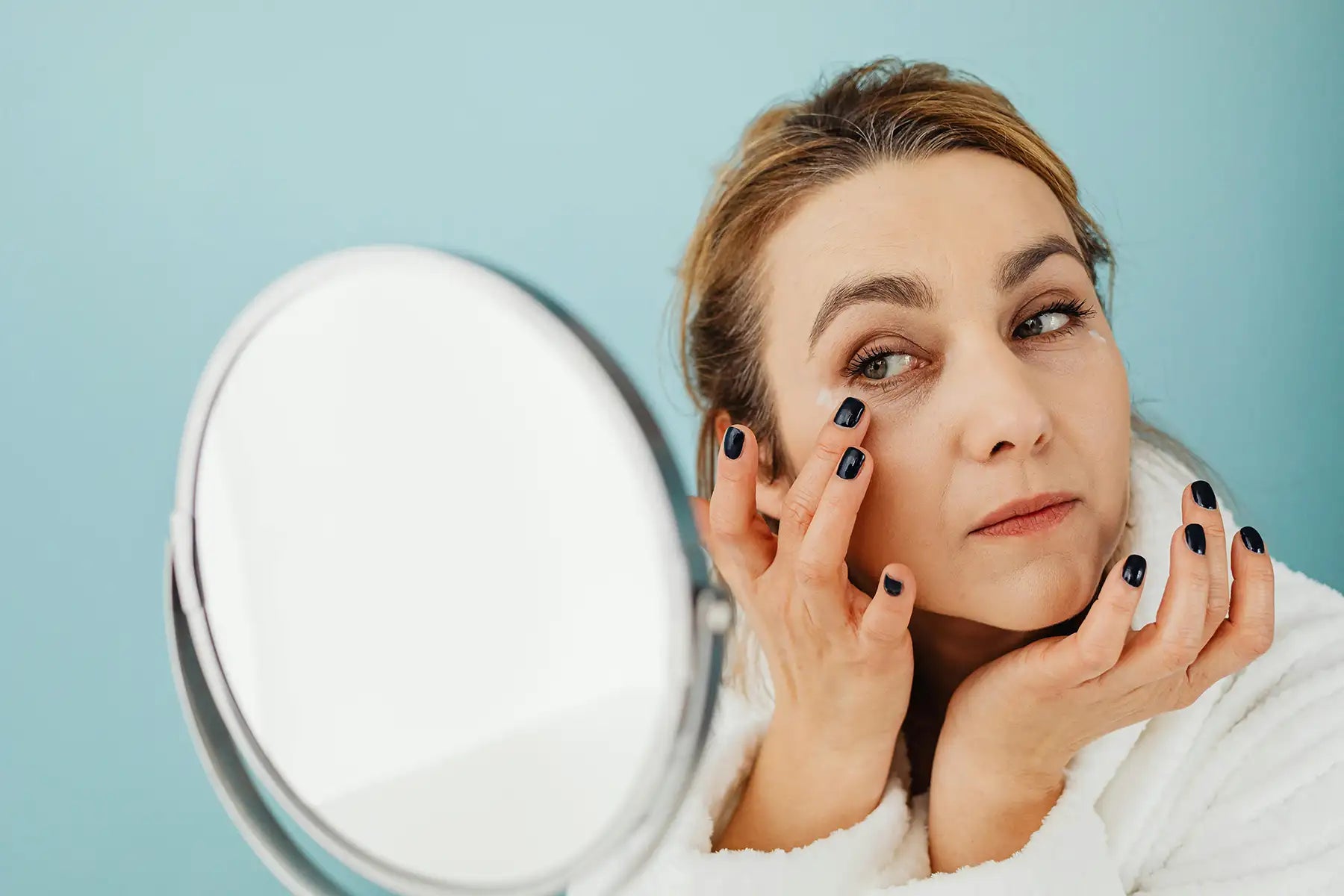 A woman looking at the mirror while applying a cream on her face
