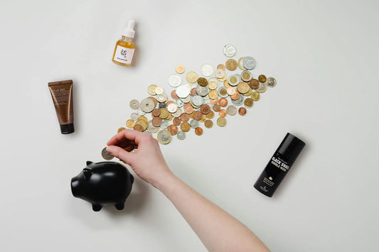 Coin being placed in piggy bank near scattered cosmetics