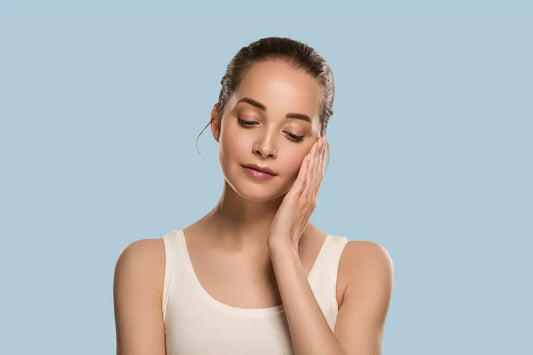 Femeie cu piele sanatoasa atingand fata pe fundal albastru