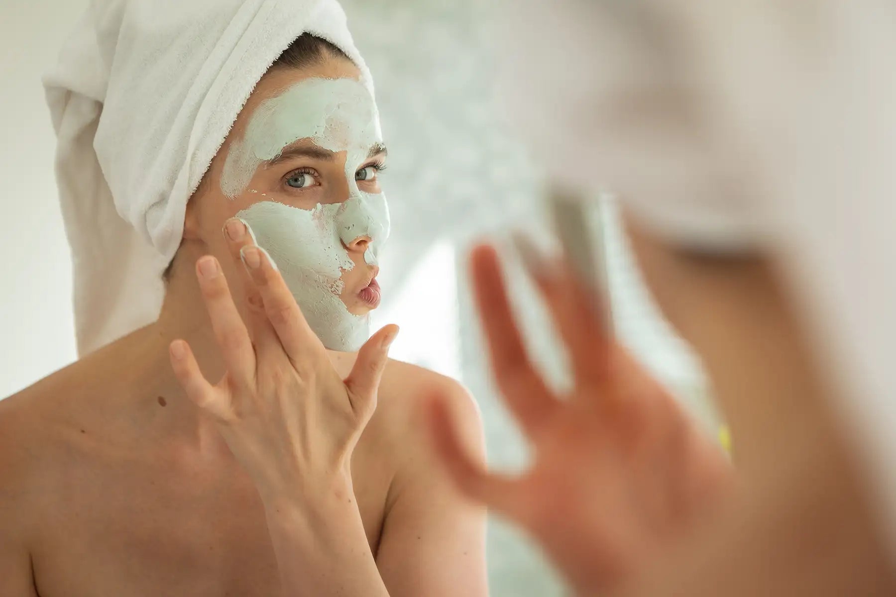 woman applying clay face mask mirror