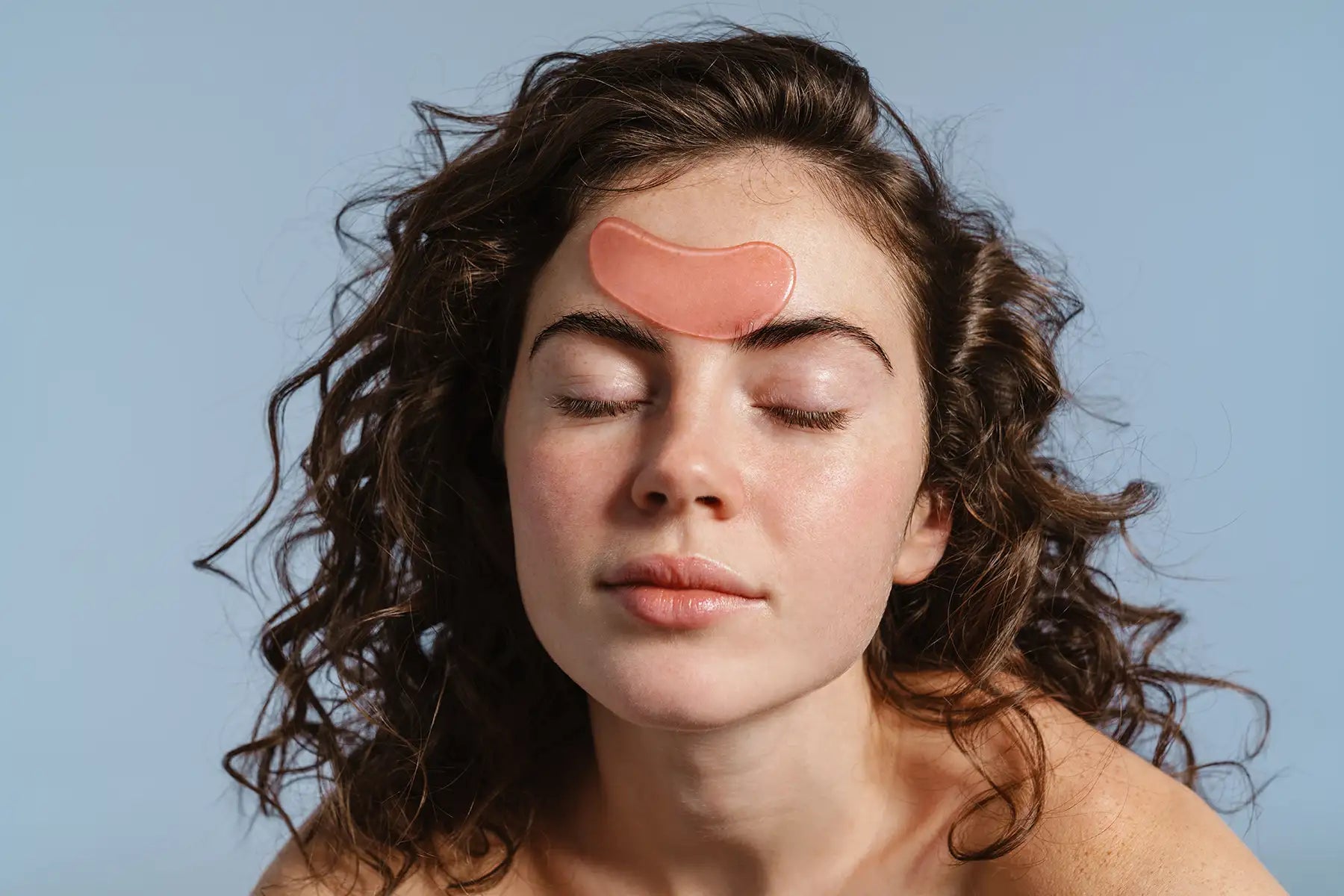 Femeie cu ochii inchisi aplicand un plasture hidrogel pe frunte pentru calmarea si hidratarea pielii