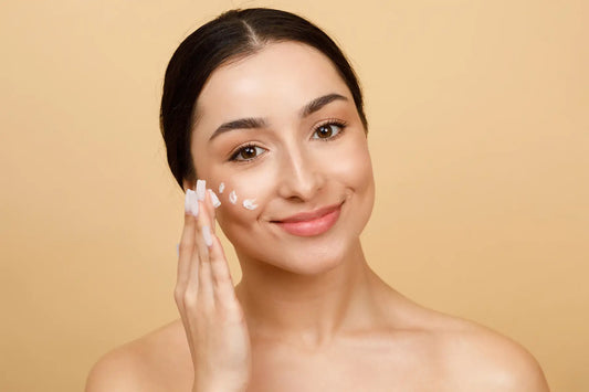 Tanara aplicand crema hidratanta pe obraz si zambind